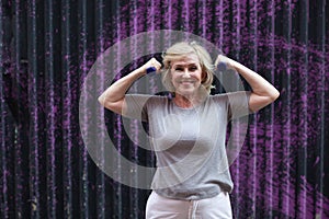 Elderly caucasian old aged woman portrait gray haired doing exercises with dumbbells outdoors.