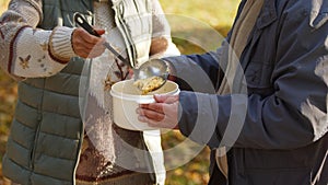 Elderly caucasian person shares her homemade soup to help the unemployed people in need.