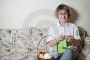 An elderly Caucasian woman knits sitting on a couch.