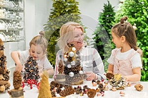 Elderly caucasian woman making pine cones decoration for christmas with two granddaughters