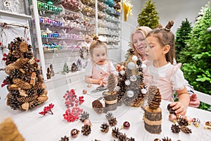 Elderly caucasian woman making pine cones decoration for christmas with two granddaughters