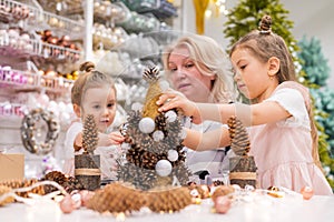 Elderly caucasian woman making pine cones decoration for christmas with two granddaughters