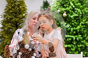 Elderly caucasian woman making pine cones decoration for christmas with two granddaughters