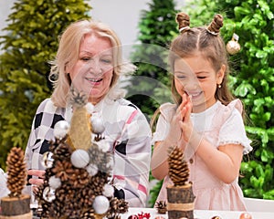 Elderly caucasian woman making pine cones decoration for christmas with two granddaughters