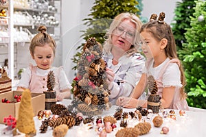 Elderly caucasian woman making pine cones decoration for christmas with two granddaughters