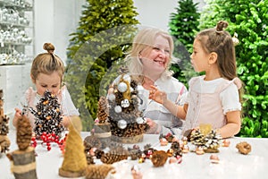 Elderly caucasian woman making pine cones decoration for christmas with two granddaughters