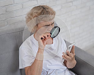 Elderly Caucasian woman with myopia and trying to read a message on a smartphone using a magnifying glass.