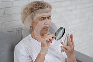 Elderly Caucasian woman with myopia and trying to read a message on a smartphone using a magnifying glass.
