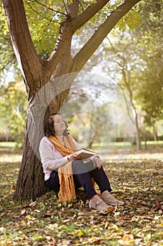 Elderly caucasian woman resting by a tree outdoors. Autumn season