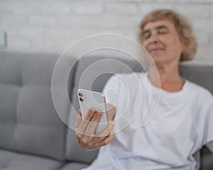 An elderly Caucasian woman suffers from farsightedness and tries to read a message on a smartphone with her arm