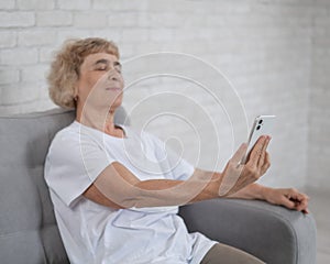 An elderly Caucasian woman suffers from farsightedness and tries to read a message on a smartphone with her arm