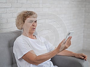 An elderly Caucasian woman suffers from farsightedness and tries to read a message on a smartphone with her arm