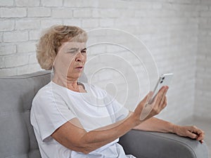 An elderly Caucasian woman suffers from farsightedness and tries to read a message on a smartphone with her arm photo