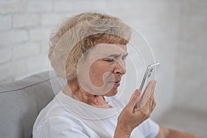 An elderly Caucasian woman suffers from myopia and tries to read a message on a smartphone.