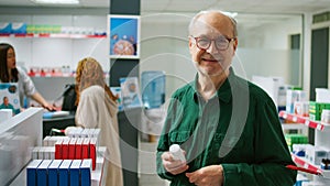 Elderly client smiling and looking at cardiology pills box in pharmacy