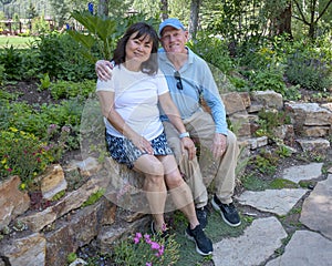Elderly couple in an affectionate pose sitting on a stone wall in a garden in Colorado.