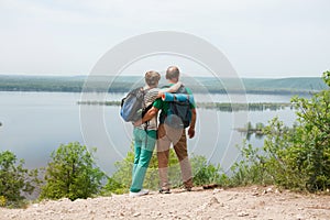 Elderly couple with backpacks travels around mountains.