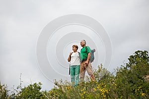 Elderly couple with backpacks travels around mountains.