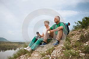 Elderly couple with backpacks travels around mountains.