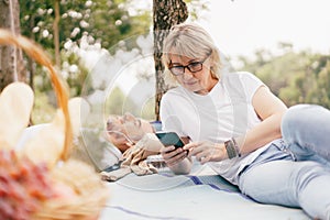 Elderly couple of caucasian using smartphone together in the park, Senior couple relax in summer daylight. relaxing concept of lif