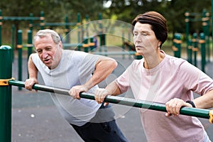 Elderly couple doing push-ups on crossbar together on sports ground of city park