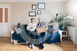 Elderly couple doing shoppings online on the sofa at home, looking at each other and smiling photo