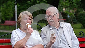 Elderly couple eating ice cream on a park bench.