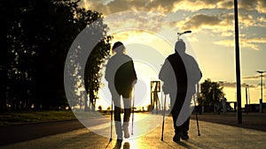 An elderly couple is engaged in Nordic walking in the park going into the sunset. A man and a woman walk with sticks to