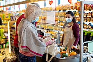 Elderly couple in face masks paying at cashdesk at supermarket