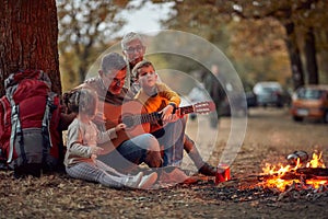 An elderly couple and grandchildren playing guitar in the forest around a campfire