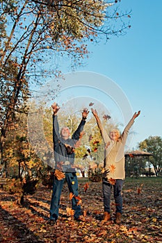 Elderly couple happily throws autumn fall leaves sitting in a park. Positive emotions of the elderly