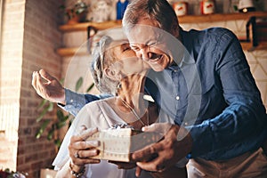 Elderly, couple and happy with gift, surprise and kiss on face together in home. Man, woman and retirement show love