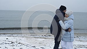 An elderly couple is having fun and dancing on the beach by the sea in winter.