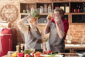 Elderly couple having fun in kitchen, playing with vegetables