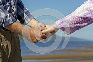 Elderly couple holding hands walking along the beach