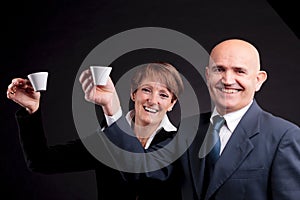 An elderly couple holding up two cups of espreso coffee