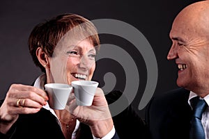 An elderly couple holding up two cups of espreso coffee