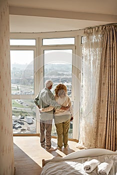 Elderly couple hug and look at city from window