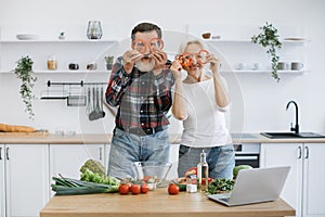 Elderly couple, husband and wife, having fun in kitchen while preparing breakfast.