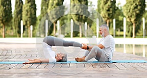 Elderly couple of husband and wife performing partner yoga, practicing Halasana on fresh air outside in sunny morning photo