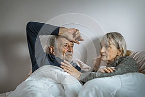 The elderly couple lie in confines on the bed, the man suffering and The woman had to comfort him