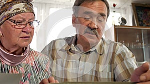 An elderly couple man and woman are looking at their old photos at home and talking. A man with a mustache, a wife with
