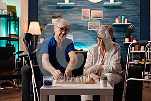 Elderly couple playing chess on board sitting at home