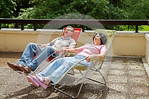 The elderly couple relax in lounges on sunny terrace