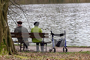 Elderly couple relaxing on a lakeside park bench with a rollator nearby