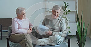 Elderly couple sits at home on couch hold papers receive documents letter with bad news,angry annoyed old man discusses
