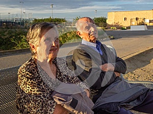 Elderly couple sitting on a bench smiling talking to someone