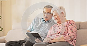An elderly couple is sitting on the couch in the living room, the husband sitting