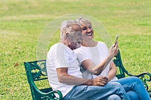 Elderly couple sitting together on bench in public park and video call with smartphone