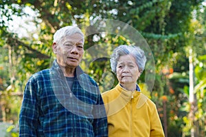 Elderly couple smiling and looking at the camera while standing in a garden. Concept of aged people and healthcare